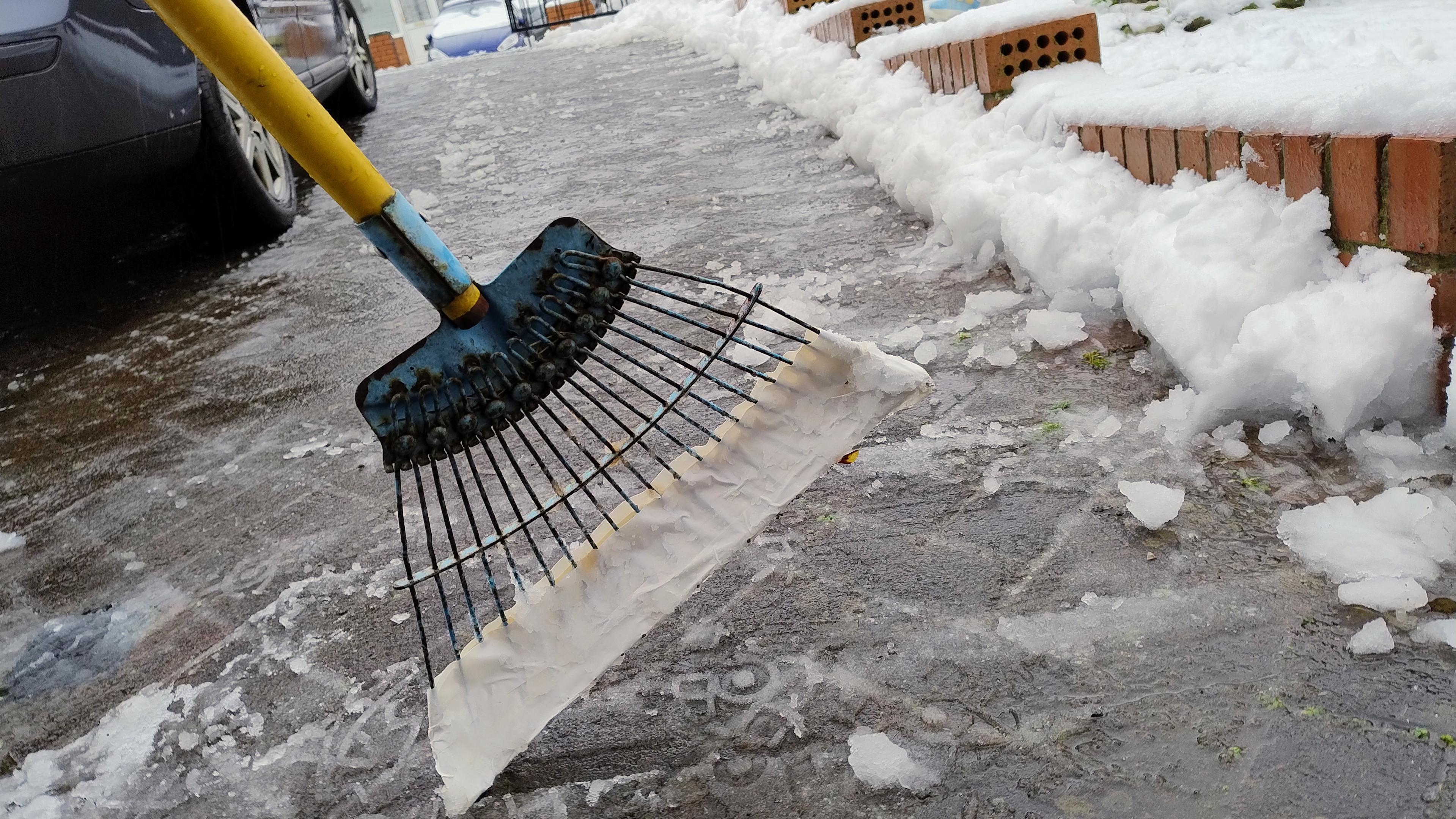 A garden leaf-rake with the prongs wrapped in white duct tape, forming an improvised snow (dragging) shovel. In the background is a successfully scraped driveway!!