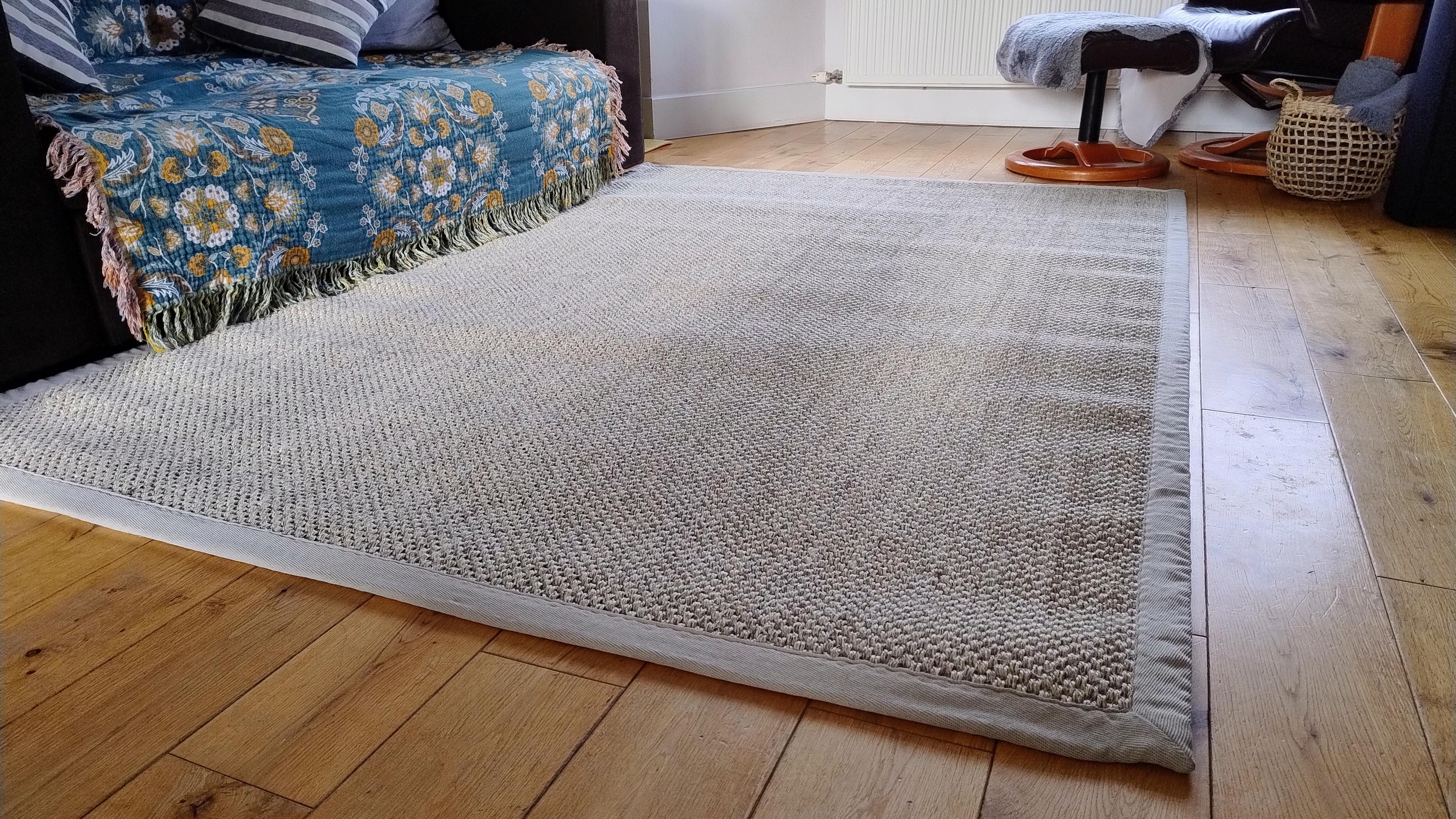 A sandy coloured natural fibre rug on a wooden living room floor.