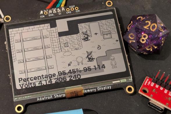 Photo of a monochrome 2.4" display showing the other attached image. A fantasy dungeon is shown with train tracks, brick walls, treasure chest. The display also shows battery health data.