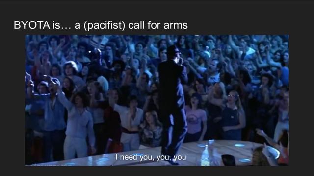 An image from the Blues Brothers movie. Dan Aykroyd back is shown while he is facing the crowd. Everyone is pointing their index fingers in the air. A subtitle shows a verse from the "Everybody Needs Somebody" song. The words are "I need you, you, you". The image is inside a presentation slide whose title is "BYOTA is... a (pacifist) call for arms"