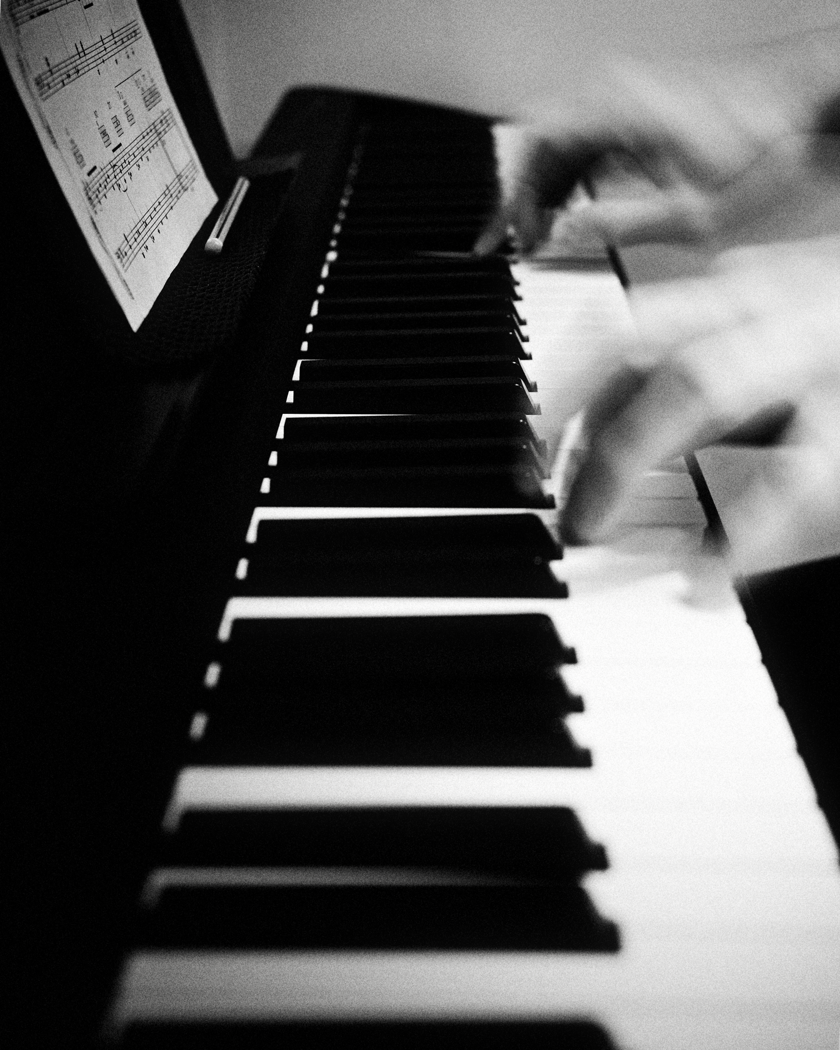 Hands with motion blur, apparently playing a piano, rendered in a grainy black and white.