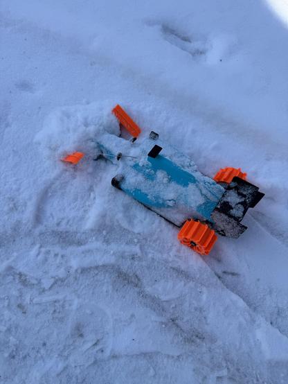 A photo of an OpenRC F1 car stuck in the snow. The front skis have flipped over, rendering it un-steerable.