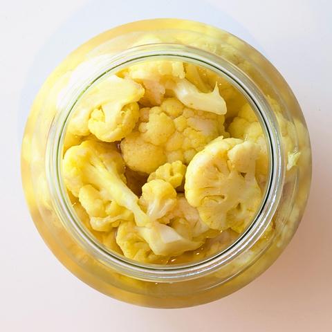A round glass jar with yellow pickled cauliflower florets.