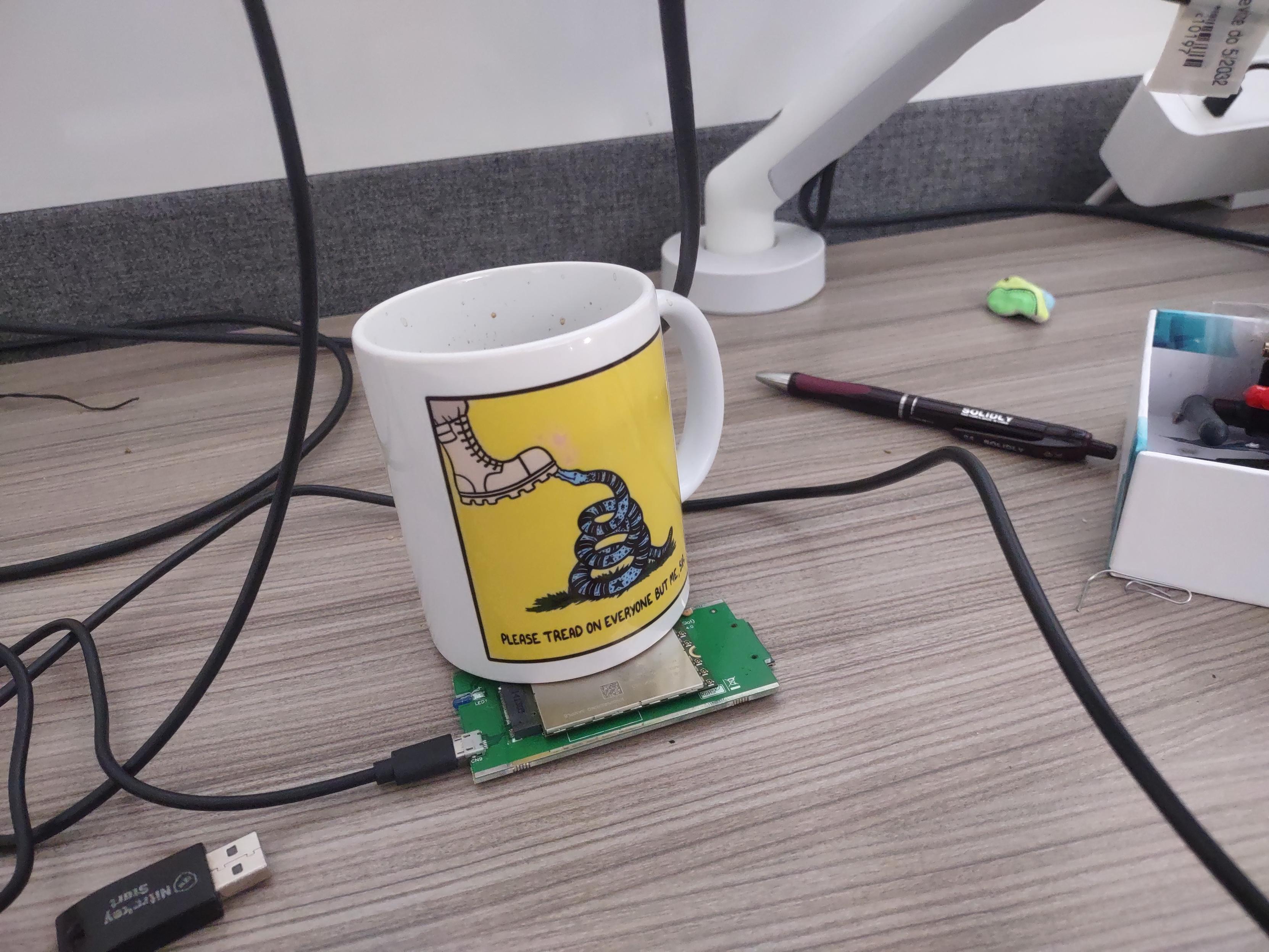 A M2-to-usb adapter with a modem board inserted in the slot. The card has a screw hole in the wrong spot, is held in place with a coffee mug.