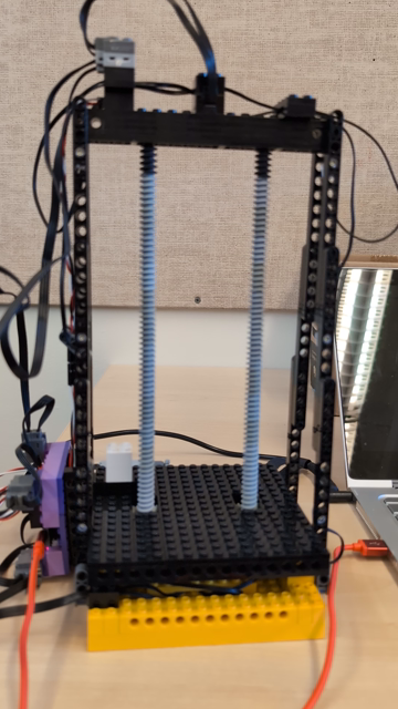 A lego model consisting of a rectangular frame holding two columns of worm gears. A platform surrounds the worm gears which is driven up and down as the columns rotate. Lights flash as the platform moves and the whole structure shakes ominously.