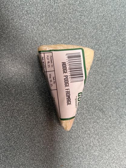 A small wedge of cheese on a green countertop with a label that read “hodge podge fromage”