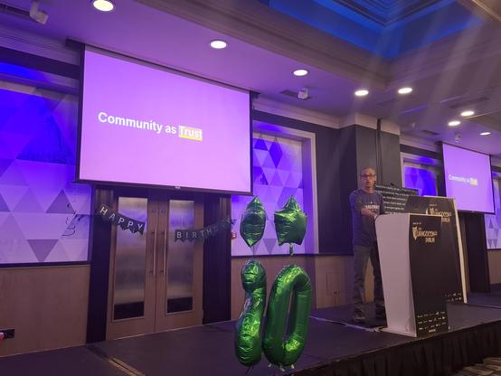 Carlton Gibson on the DjangoCon Europe stage and slide with "community as trust" sentence.