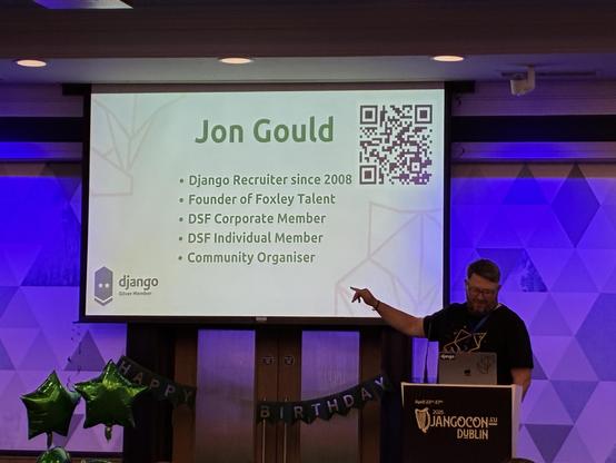 Jon Gould to the right of his slides. He points towards the slides with the "django silver member" badge in the bottom right of the slide