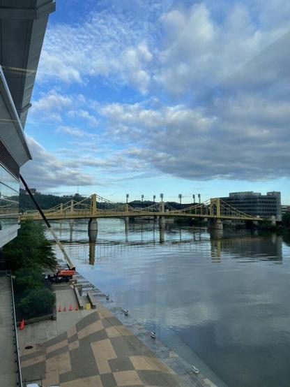A view of the river from the Pittsburgh Convention Center, with a view of blue skies and white clouds reflected in the water, crossed by yellow bridges.