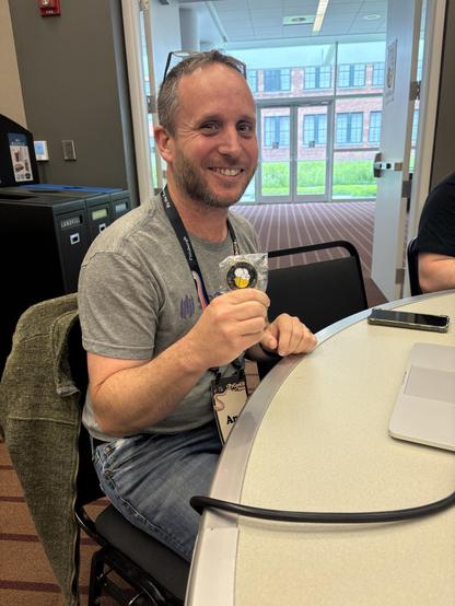 A man sitting at a table holding a BeeWare challenge coin. 