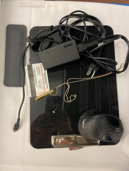 A black clipboard, a logitech mouse, a wrist rest, a stud earring, a whistle necklace, and a computer power cord, and a parking card. 