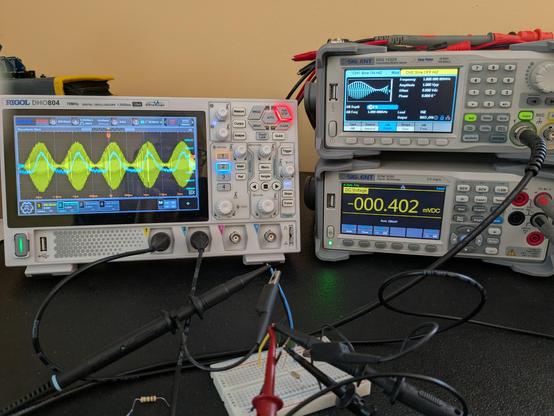 An oscilloscope showing AM demodulation next to a signal generator (producing the signal) and a digital multi meter (not used for this). In the foreground is a breadboard circuit with probes and leads connected.