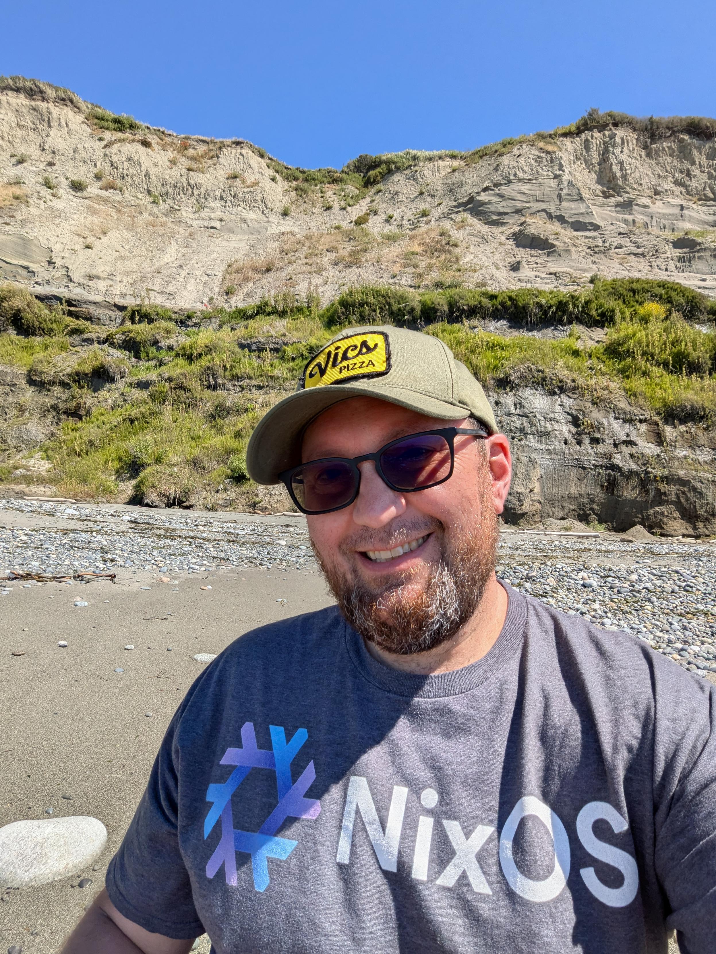 Guy sitting on a beach wearing a NixOS shirt