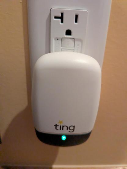 A small device (approximately 4" by 2") plugged into an electrical outlet. A small green light appears at the bottom under the label "ting".