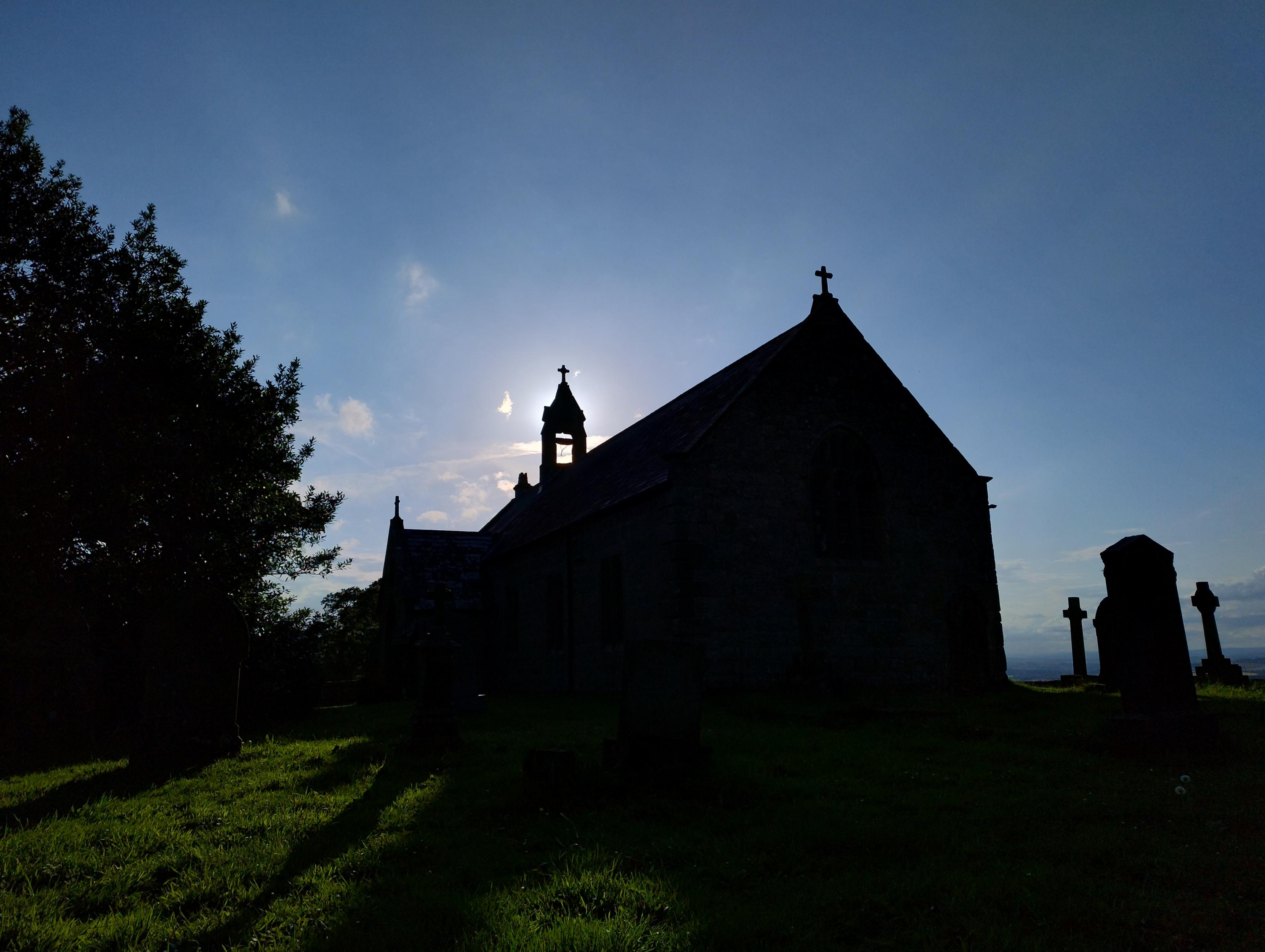 Small rural church in silhouette with the sun behind the bell.
