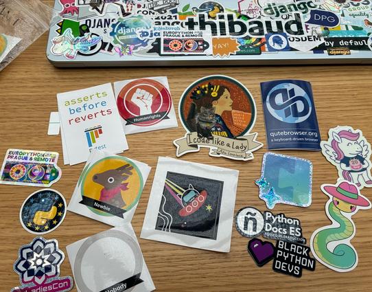 Close-up of Python community stickers on a table, with EuroPython, PyLadiesCon, Ada Lovelace, Python Docs ES, Black Python devs, qutebrowser, Django pony