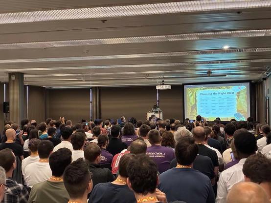 full conference room with a speaker in the background and their slides about 'choosing the right orm', in the foreground we see attendees from the back