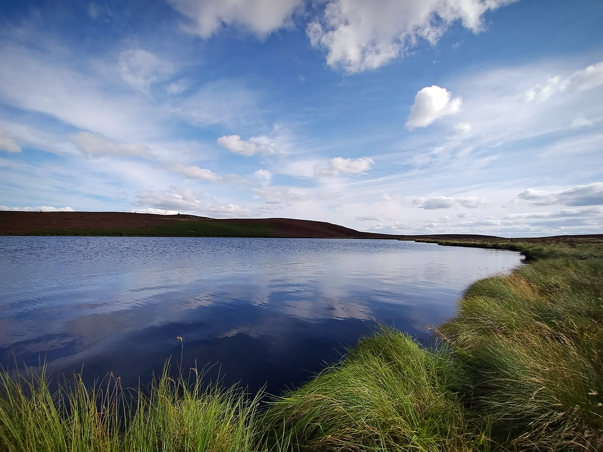 Photo of a remote moorland lough (lake) under a mostly blue sky.