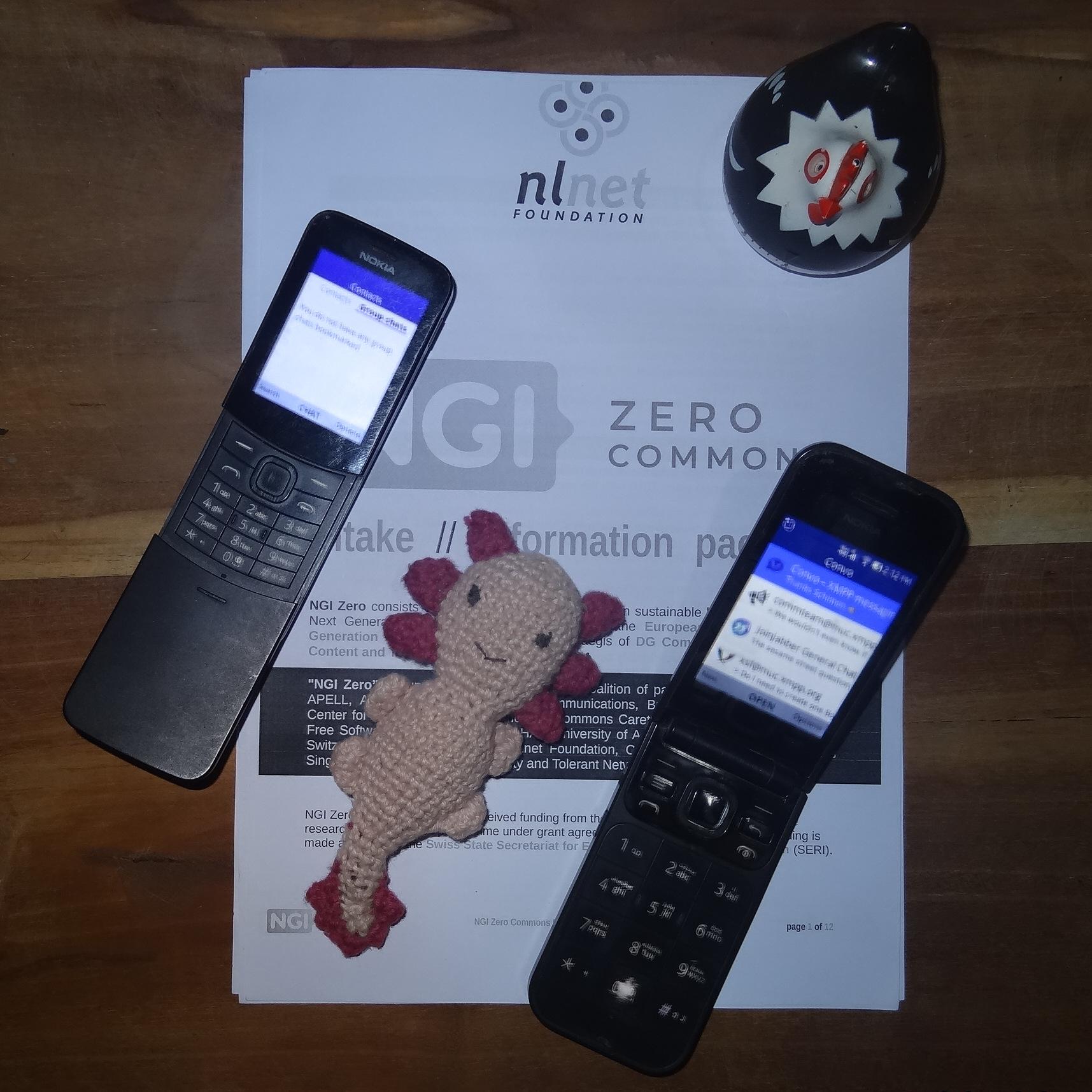 A printout of an NGI Zero Commons fund information document, with a few things placed on top. Diagonally from top left to bottom right are: A Nokia 8110 "Bananaphone", an amigurumi (crochet) axolotl, and a Nokia 2720 Flip phone. On the top right corner of the paper is a round clockwork hen named clock-a-doodle-doo.
Both phones are running the Convo app: one with an empty group chat list, and another with a list of conversations. If you look closely and get past the pixellation and blurred-ness, you might recognise group chats with icons for: Convo, XSF Communications Team, XSF Discussion, and JoinJabber General Chat. A printout of an NGI Zero Commons fund information document, with a few things placed on top. Diagonally from top left to bottom right are: A Nokia 8110 "Bananaphone", an amigurumi (crochet) axolotl, and a Nokia 2720 Flip phone. On the top right corner of the paper is a round clockwork hen named clock-a-doodle-doo.
Both phones are running the Convo app: one with an empty group chat list, and another with a list of conversations. If you look closely and get past the pixellation and blurred-ness, you might recognise group chats with icons for: Convo, XSF Communications Team, XSF Discussion, and JoinJabber General Chat.