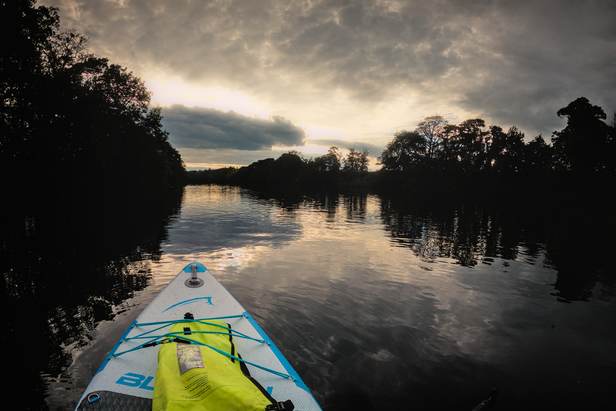 View from a paddleboard, towards the sun - shortly before sunset, on a tree lined river.