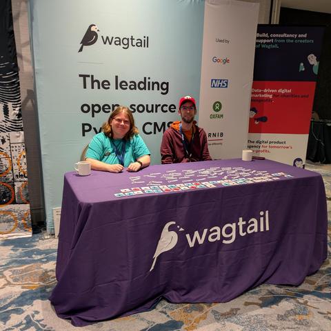 Meagen and Scott are sitting at the Wagtail booth and smiling with stickers spread out in front of them.