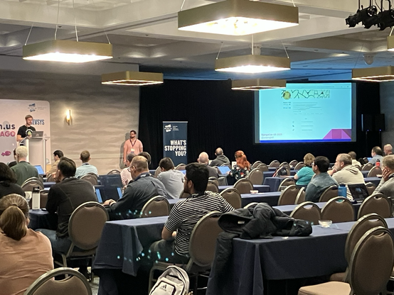 On the left is Adam G Hill at the podium. To the right is the projector screen with a slide on the BeeSocial app, which utilizes SQLite.