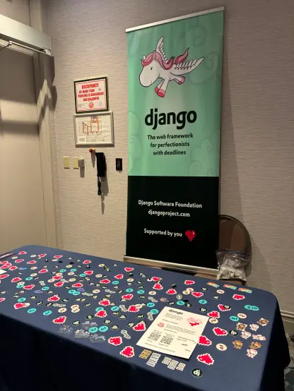 Photo of the Django Software Foundation booth setup, with a table covered in stickers, a conference banner with the Django pony