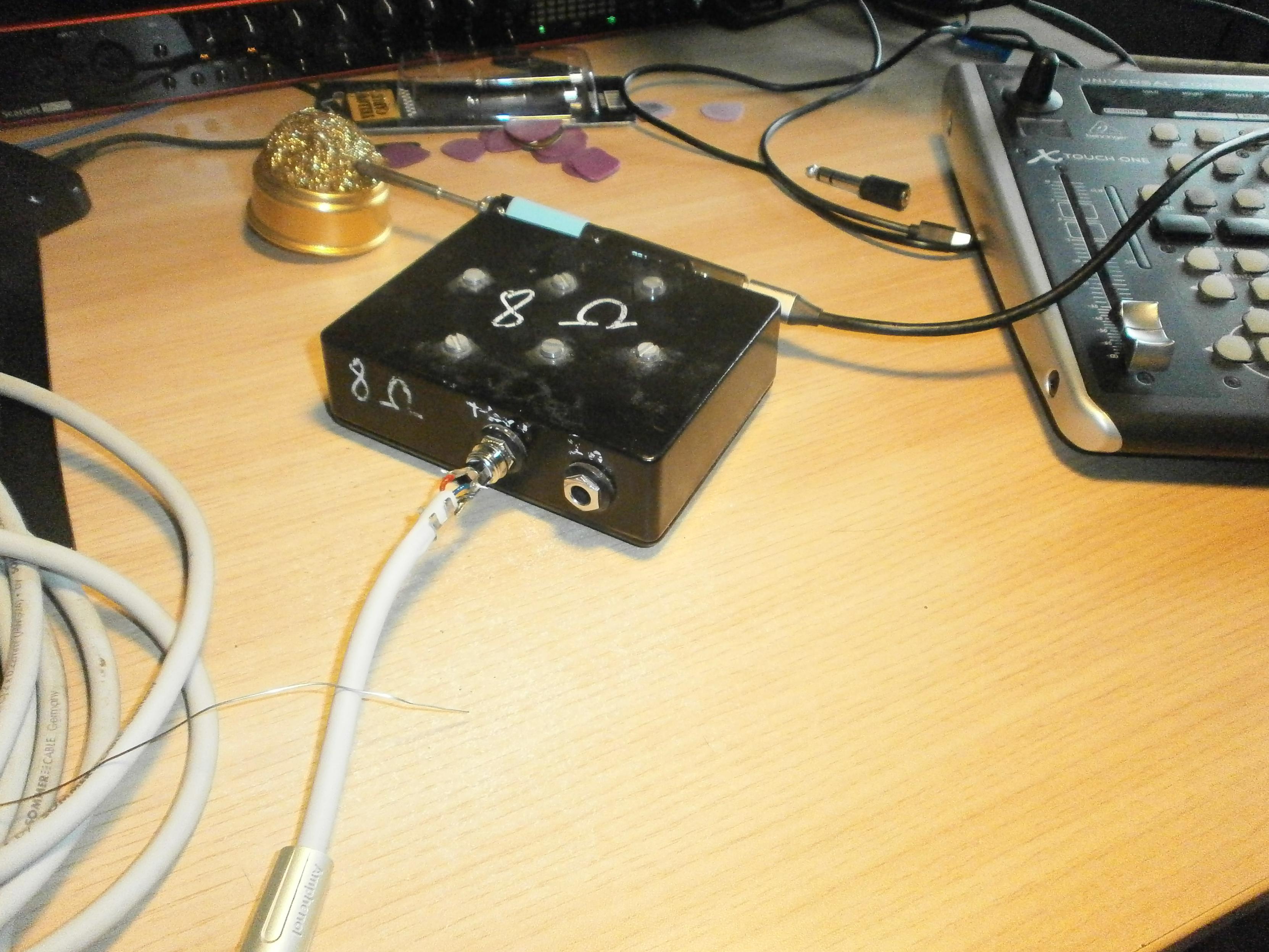 A jack connector is being soldered onto a cable; the connector is plugged into a black box, a soldering iron is visible in the background.