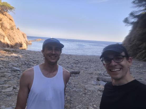 Me and Simon smiling on the beach with blue water and cliffs in the background.