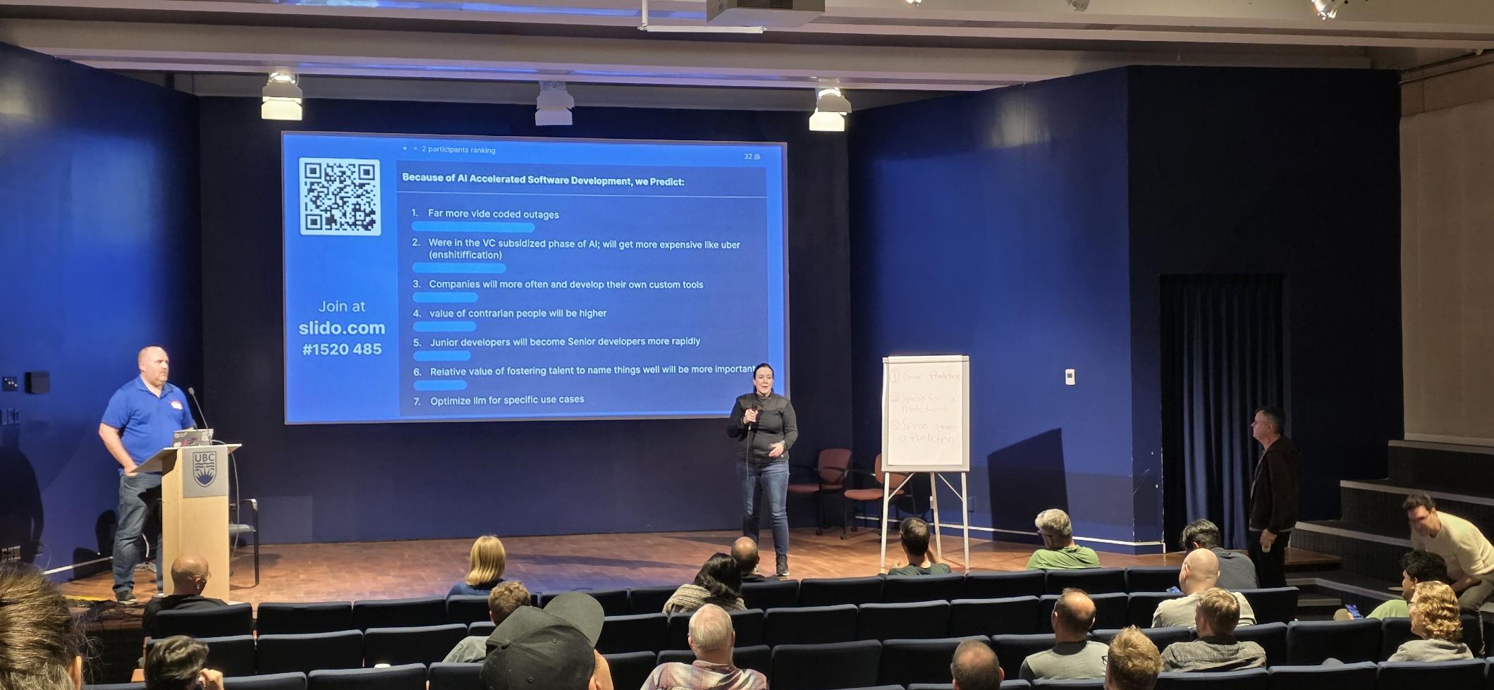 Main stage of the conference, a person speaking on a mic with presentation slide behind showing the predictions and voted on slido