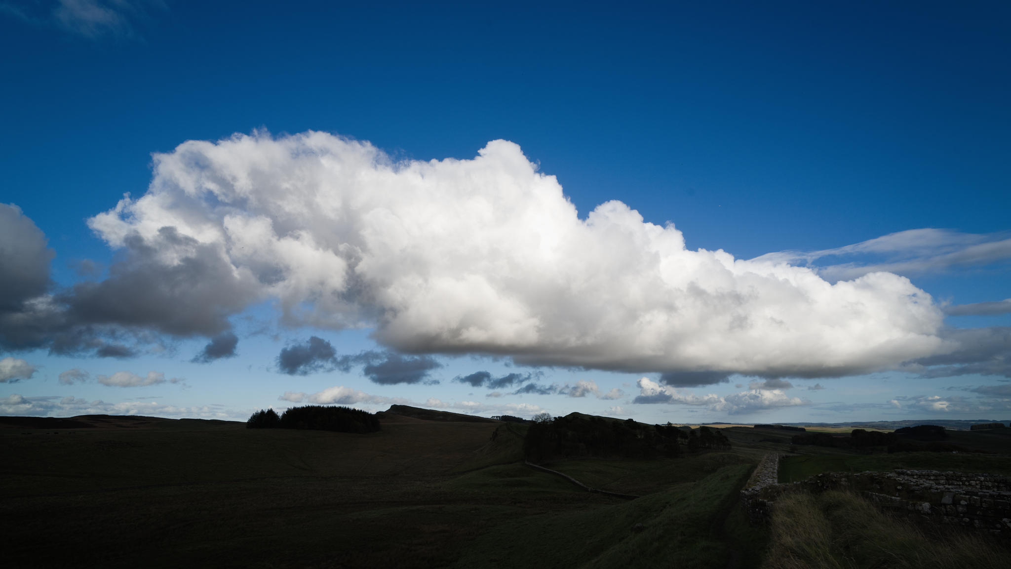 Large white cloud in a blue sky. Image has been exposed for the cloud, and the ground is almost dark.