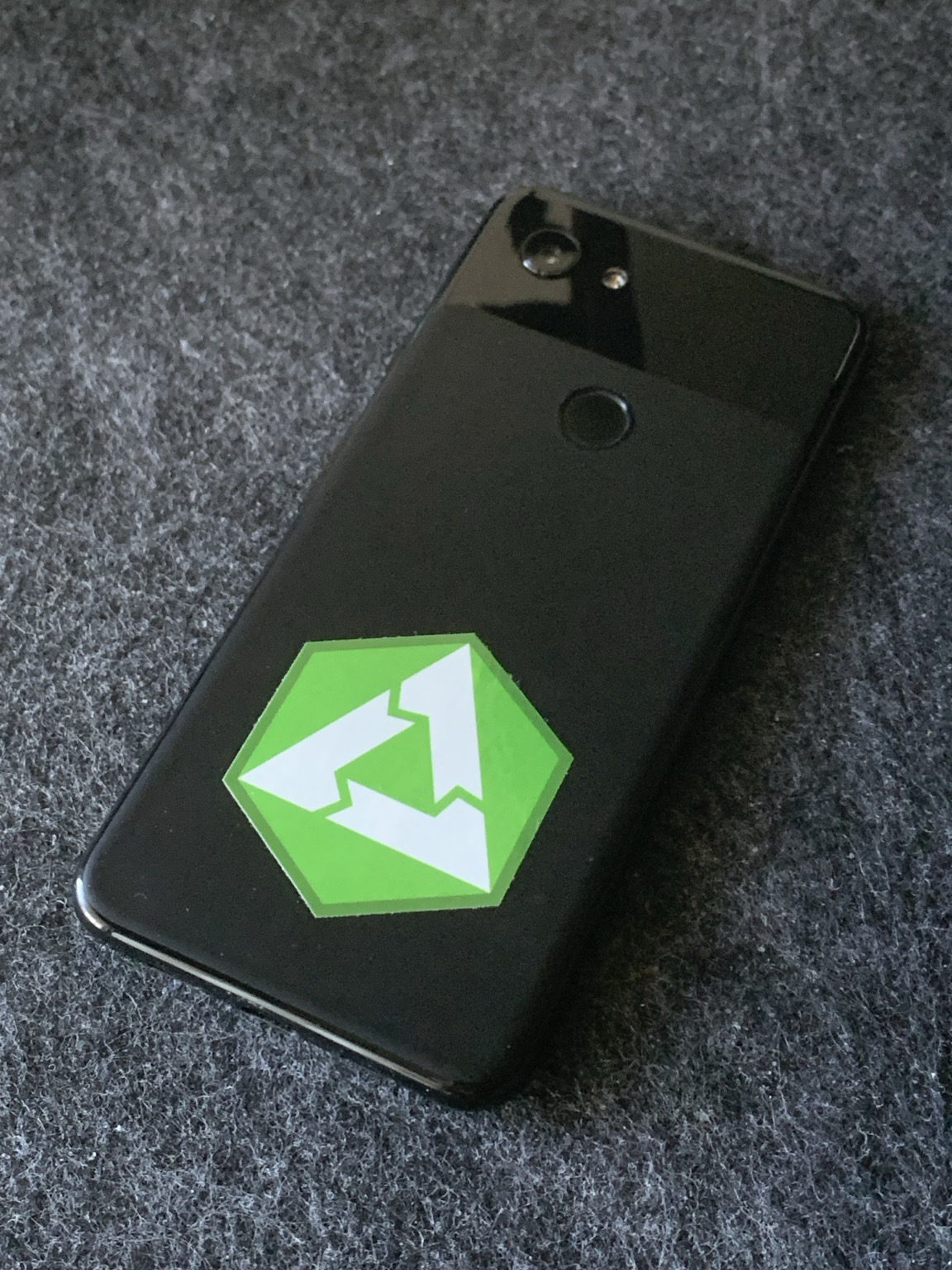 A Google Pixel 3a phone on its back with a postmarketOS sticker on it.