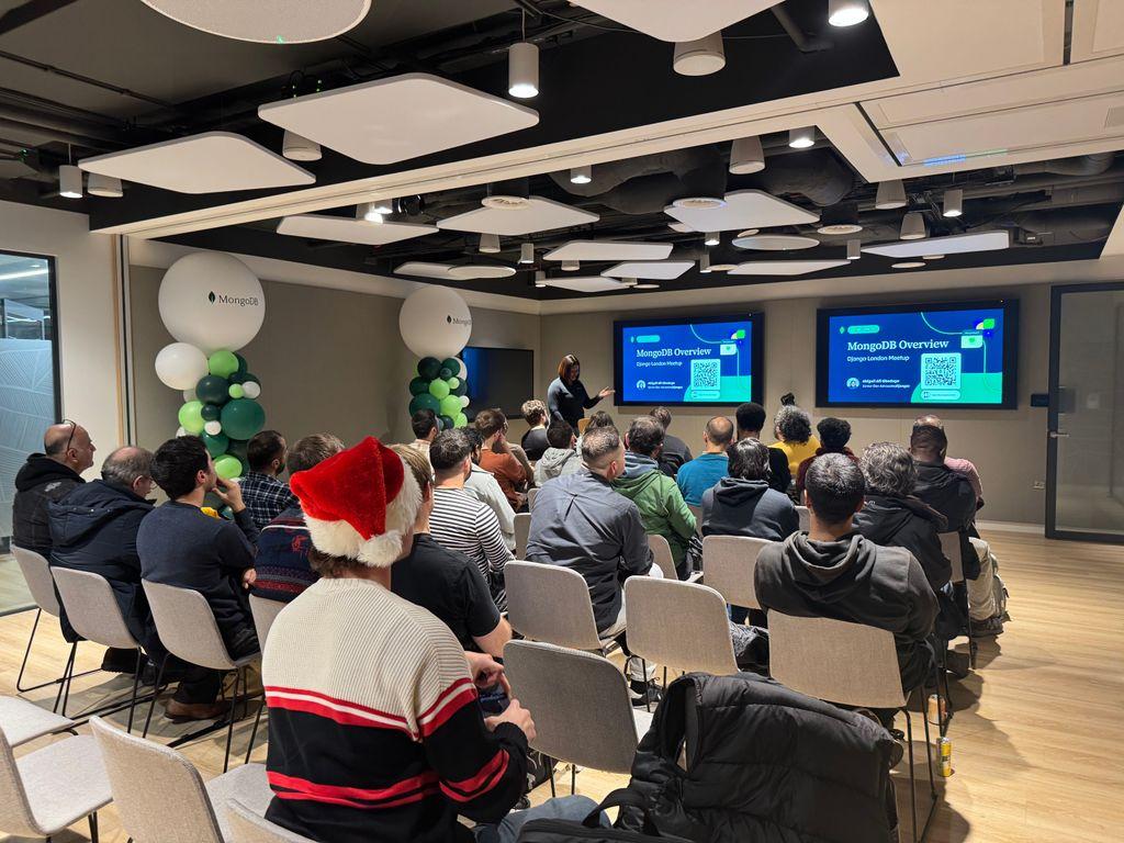 Audience seated at the Django London Meetup in the MongoDB event space, watching speaker Abigail Afi Gbadago present a “MongoDB Overview” talk on large screens, with MongoDB-branded decor and a festive December atmosphere.