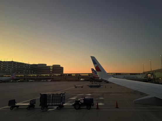 Two American Airlines planes at an airport gate during sunset.
