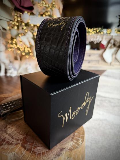 A black box with a tire on top. The tire has gold writing on it. The box has gold writing on it. The background is blurred.