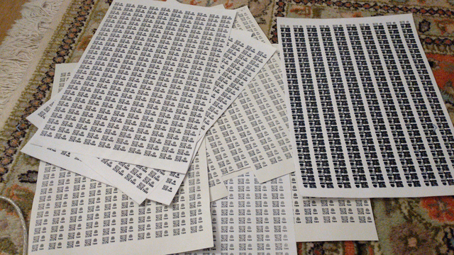 several sheets of A4 paper, all of them printed full of little QR Codes with the monochrome Text "👛 Yann" next to them. The rightmost one is completely messed up with several QR codes printed over each other.