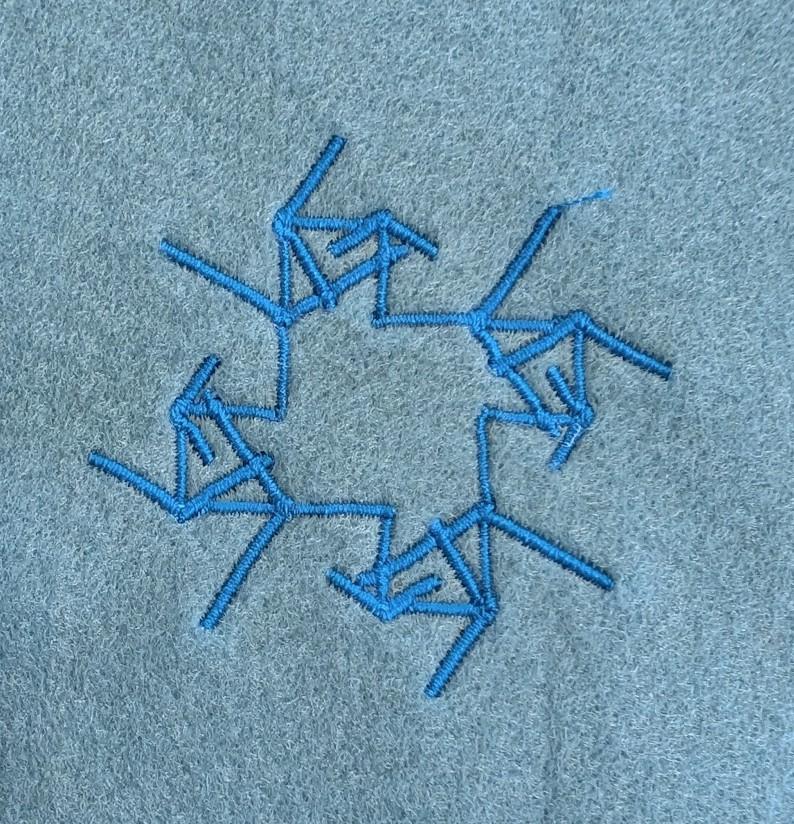 A pattern stitched onto fabric, its like a square, made up of angular lines jutting out at both sides of the square.