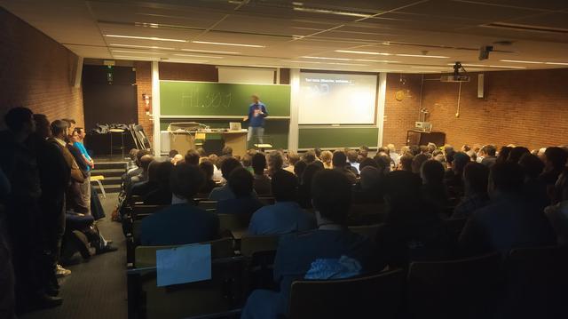 A packed room with Yorik on stage giving a presentation. 