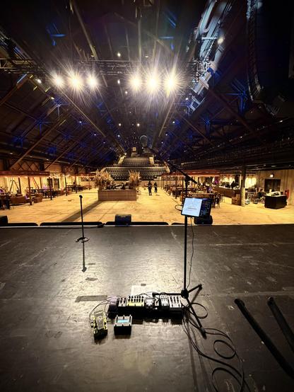 A stage with a soundboard and lights in a large hall with tables and chairs.