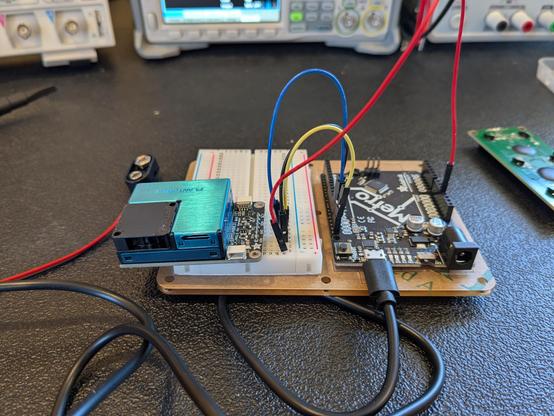 A small blue metal and black plastic box mounted on a circuit board which is connected by 4 wires to a Metro Arduino board.