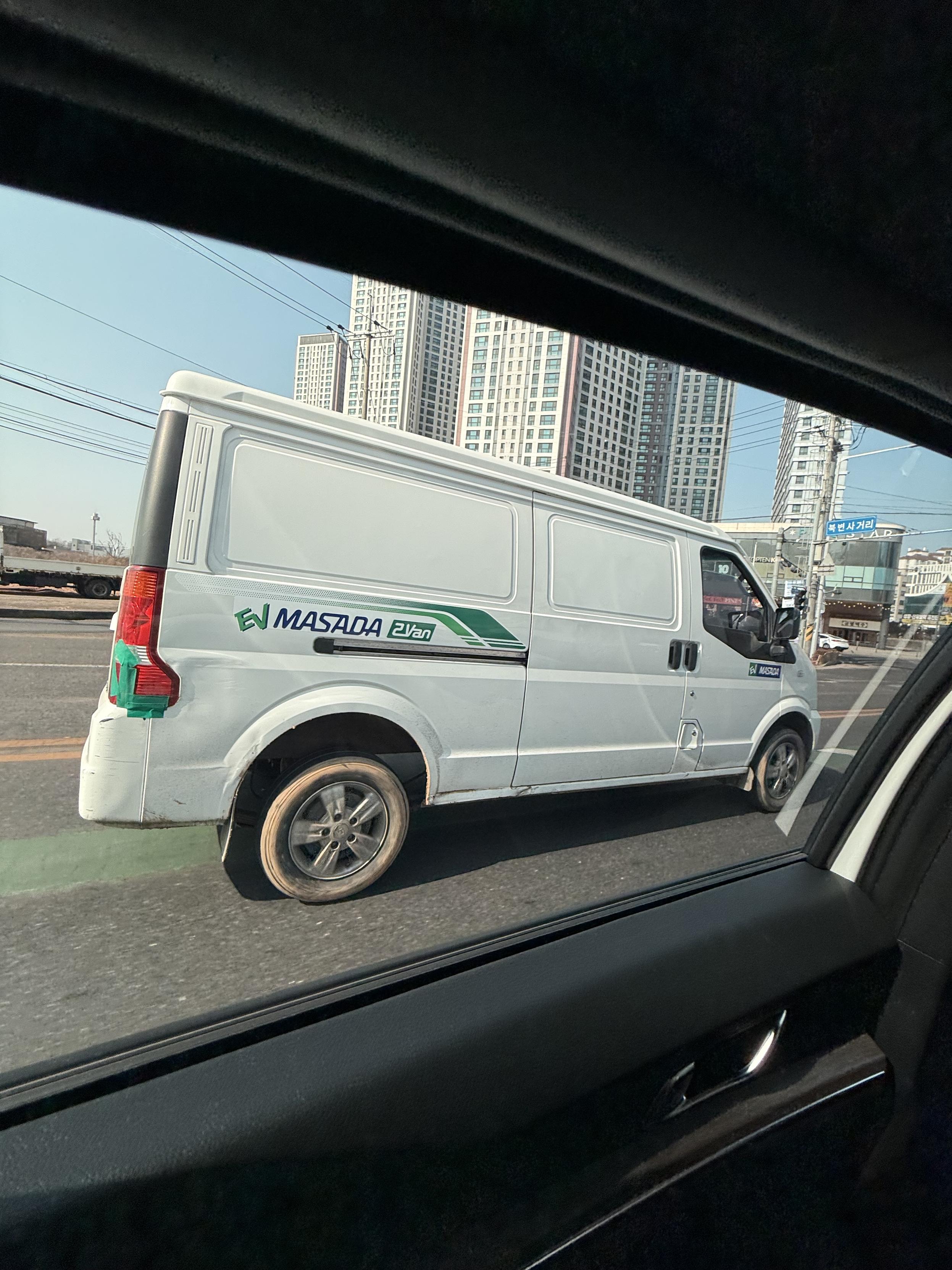 An EV Masada 2 fan. White. Looks like a box except for the curve down for the windshield. The tires are caked in mud. The right tail light is held together with green duct tape.