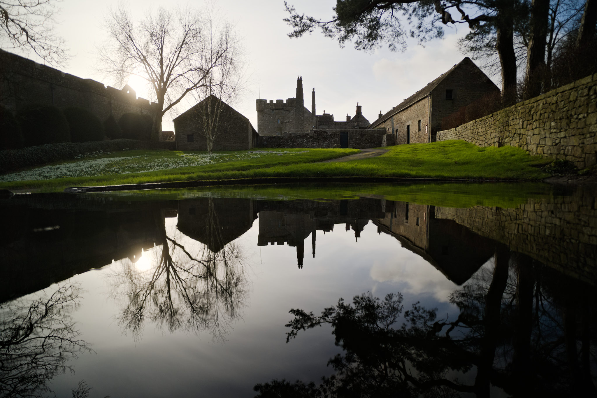 A fortified manor reflected in a village pond.
