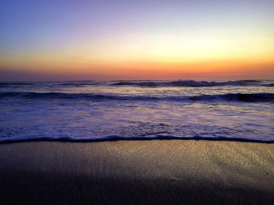 A beach with waves under a colorful sunset sky.