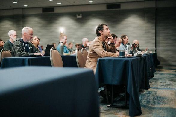 Attendees sit in rows at DjangoCon US 2025 watching a talk and taking notes non laptops
