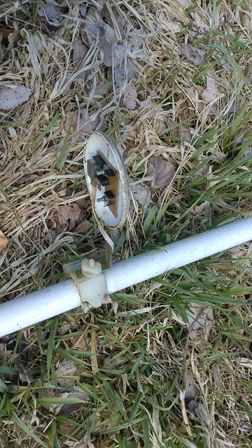 a little frisbee with sensors underneath, mounted with a 3d printed bracket to a white pole laying on grassy ground. The frisbee cracks (after years of exposure to the elements), but the 3d printed PETG parts are flexible and strong as ever.