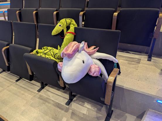 Large Python and Django pony plushies, sitting in an auditorium chair, attending the conference
