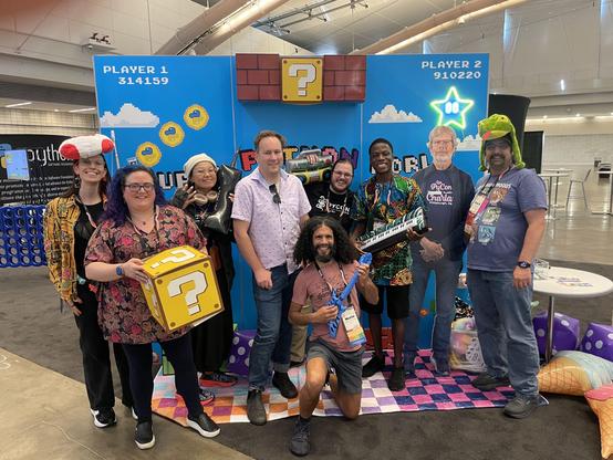 Group of posing and smiling Pythonistas in the PSF Booth at PyCon US 2025. 
