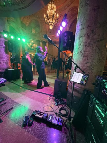 My mic stand and guitar pedals are in the foreground, bathed in green and purple light, next to a massive marble pillar in the gorgeous neoclassical rotunda, with mural panels and a staggering chandelier hanging above