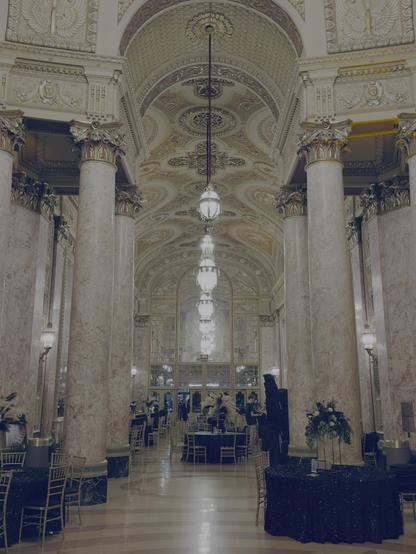 Entrance that leads to the rotunda of the Rialto, with event tables and chairs set up. Massive neoclassical pillars rise to an arched roof. The marble, plaster relief, painted panels, and gold leaf everywhere remind one of the Vatican.