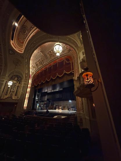 View of the stage from the side of the theatre, where we can see the orchestra pit and the red curtain which is currently lifted to show a stage space
